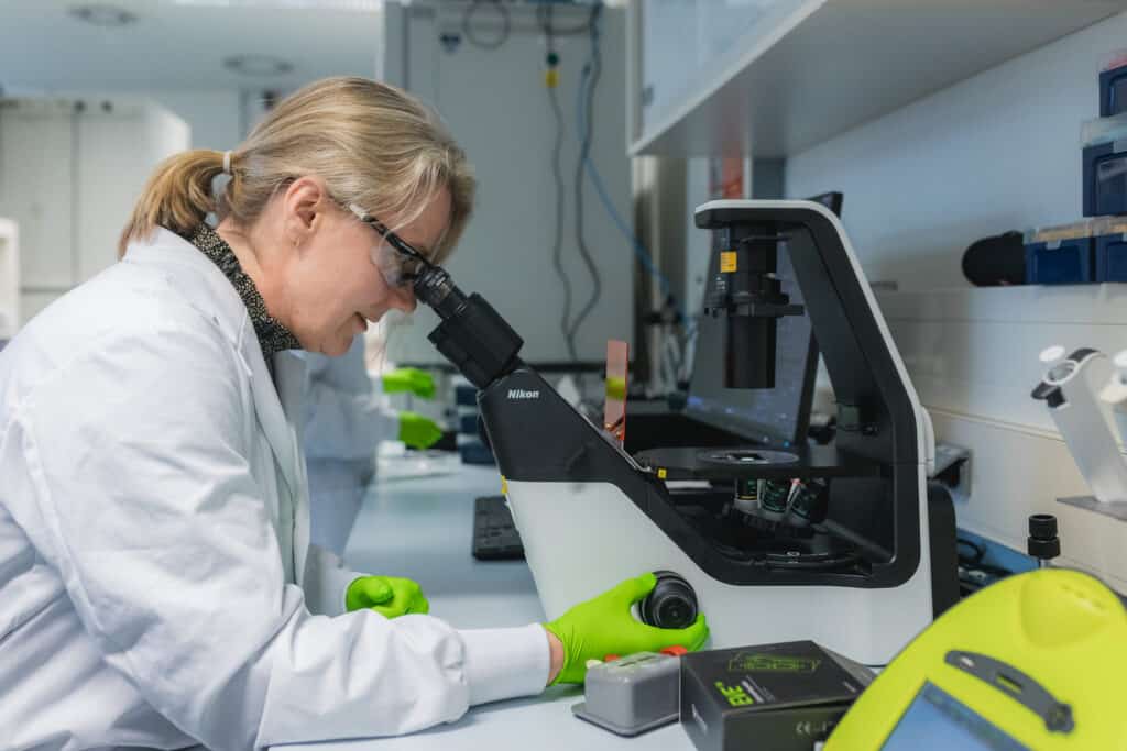 vrouwelijke onderzoeker kijkt door geanvenceerde microscoop
