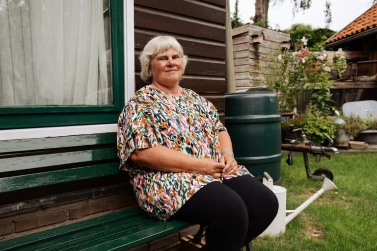 Trudie vd Graaf zit op een bankje in de voortuin